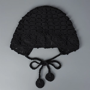 Détail du bonnet au crochet noir avec motifs ajourés et glands à pompons doux