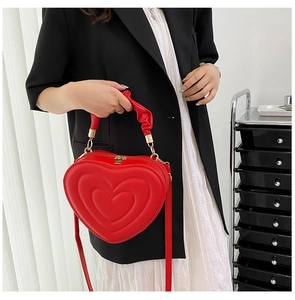 Detail of red heart-shaped handbag with concentric textures and pleated handle worn by model