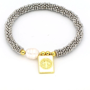 Detail of bohemian elastic bracelet featuring silver beads, irregular pearl and gold cross pendant