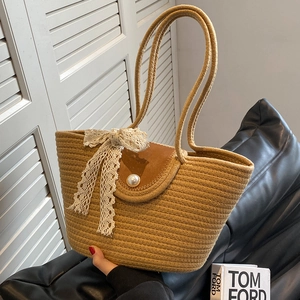 Brown woven straw tote bag with lace bow and pearl buckle on black leather sofa