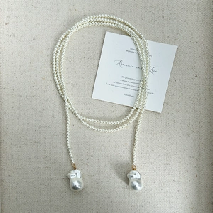 Detailed view of long pearl necklace with large baroque drops on beige fabric