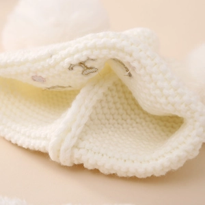 Close-up of white knit baby hat showing thick texture and soft pom-poms details