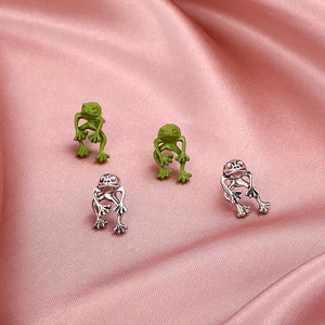 Detail of vintage metal frog stud earrings in green and silver on pink satin silk