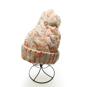 Close-up of thick cable knit winter hat with colorful mixed yarn and white faux fur pompom