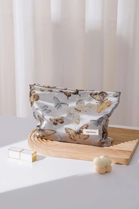 Detailed view of silk butterfly makeup bag with brand label on a wooden display stand
