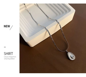 Detail of silver avocado pendant on a sleek snake chain over a textured background