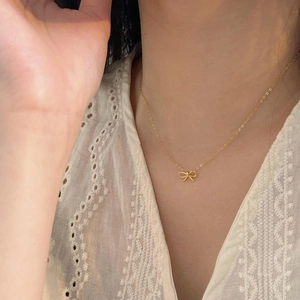 Close-up of a minimalist golden bow necklace worn on a white lace fabric background