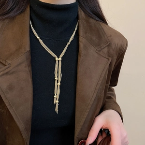 Close-up of a layered gold tassel necklace with small beads worn by a model over a black top