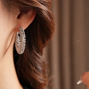 Macro shot of silver wide hoop earring with crystal pave settings worn by a model