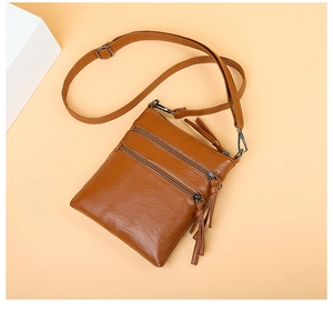 Detailed view of brown leather crossbody phone bag with dual tassel zippers and strap