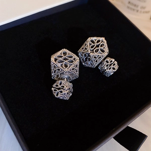 Macro shot of silver hollow geometric earrings with vintage flower pattern on black velvet