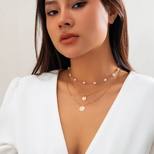 Detail of layered gold necklace with white pearls and round pendants on model