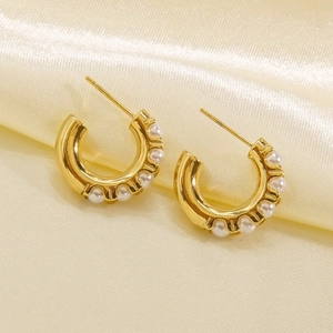 Close-up of gold C-shaped hoop earrings with embedded white pearls on silk background