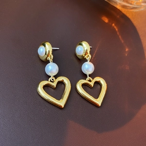 Detailed macro view of heart-shaped pearl drop earrings with elegant gold-plated finish