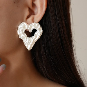 Dettaglio di orecchini a cuore d'argento irregolare indossati con stile minimalista
