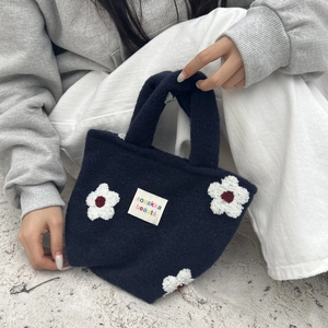 Detail of navy plush tote bag with white fleece flowers and a woven label
