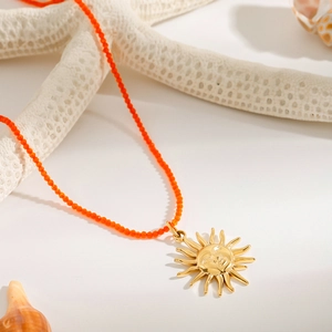 Detail of a golden sun pendant necklace with orange beads on a beach-themed background