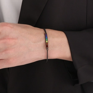 Close-up of a black woven stainless steel bracelet with a rainbow enamel bar on wrist