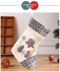 Detail of knitted Christmas stocking with snowman patch and grey plaid accents on a tree