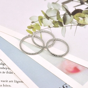 Detailed view of three silver beaded texture rings stacked on a minimalist magazine background