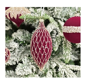 Detailed view of burgundy velvet Christmas ornaments with gold glitter mesh on a snowy tree