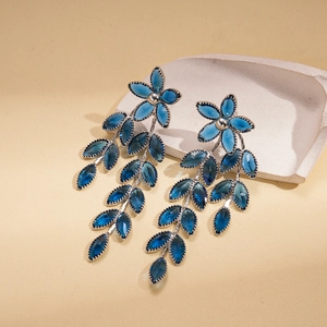 Detailed close-up of vintage blue glass flower earrings with leaf tassel on stone