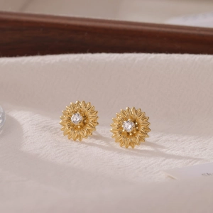 Elegant gold sunflower stud earrings with white zircon on white textured fabric