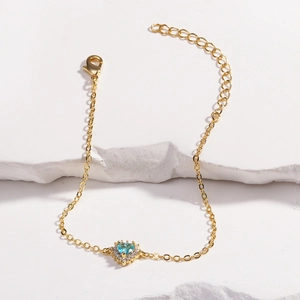 Détail d'un bracelet doré avec pierre de zircone bleu clair en forme de cœur et strass