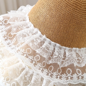 Detailed view of the woven straw hat featuring white lace trim and floral embroidery