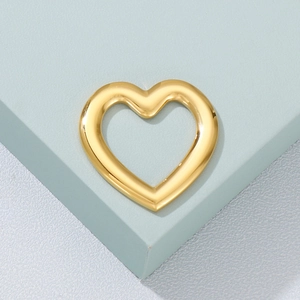 Polished golden heart-shaped metal pendant charm displayed on a minimalist pedestal