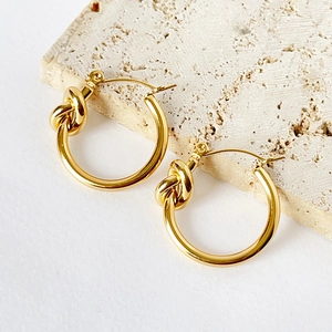 Detailed view of 18k gold plated knot hoop earrings on a textured stone surface