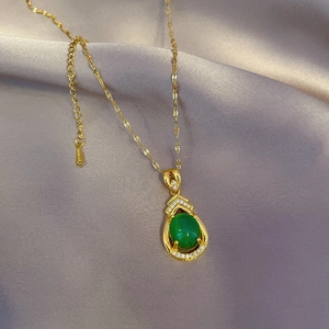 Nahaufnahme einer goldenen Edelstahlkette mit grünem Tropfenstein auf grauer Seide