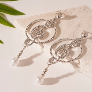 Silver treble clef earrings with diamonds and pearl pendant on a stone background