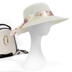 Detail of wide brim straw hat with purple floral ribbon bow on white mannequin head