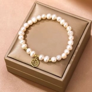 Detailed view of white freshwater pearls with a gold Fu character charm on a jewelry box