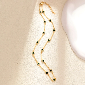 Detail of a gold plated necklace with small green heart charms on a textured background