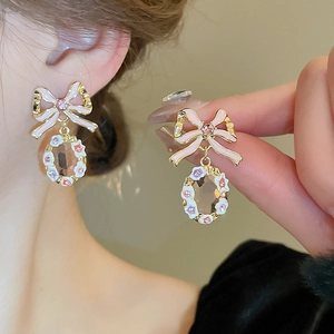 Close-up of pink bow earrings with clear gem drops and delicate floral enamel details