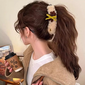 Detail view of a plush beige banana hair clip with a brown bear and yellow bow on a ponytail