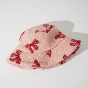 Close-up of thick pink faux sherpa bucket hat featuring red bow pattern and soft texture