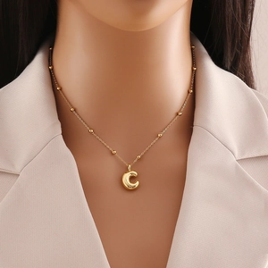 Close-up of golden letter C pendant with beaded satellite chain on a model neck