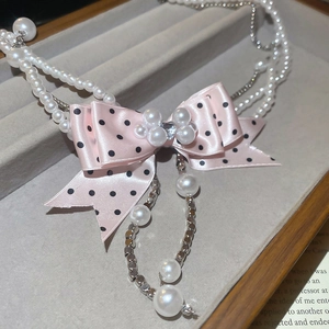 Detailed close-up of pink polka dot bow necklace with pearls and heart crystal
