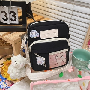 Gros plan sur le sac bandoulière en toile noire avec écusson et breloque ours