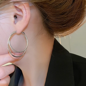 Close-up of double-layer silver cross hoop earrings with pavé crystals on a model