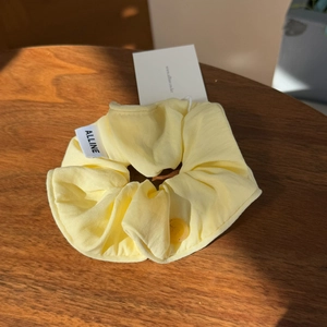 Detailed view of yellow cream puff scrunchie with brand label and button on wood