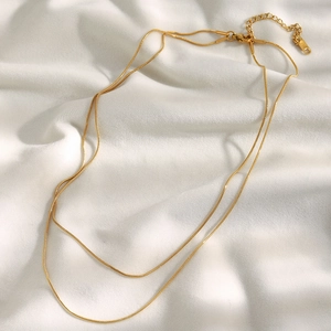 Detail of 18K gold-plated double-layer snake chain necklace on white silk fabric