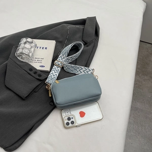 Blue PU leather crossbody square bag with a geometric wide strap on a grey blazer