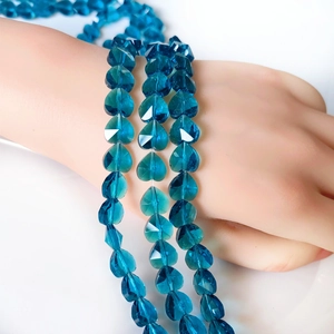 Detailed view of peacock blue faceted crystal heart beads on a hand model for DIY