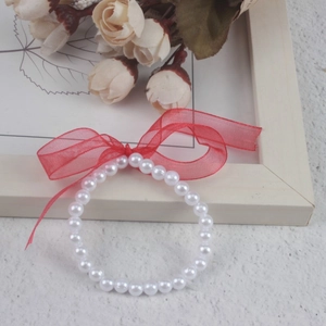 Detailed shot of children's white faux pearl bracelet with red organza bow decoration