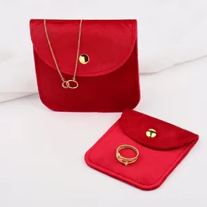 Red velvet jewelry pouches with gold metal snap buttons on elegant white silk background