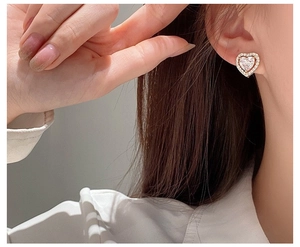 Close-up of heart-shaped gold earring with white zircon inlay on model's ear